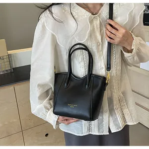 Detail of black leather bucket bag with top handles and adjustable shoulder strap worn by model