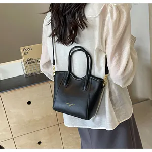 Detail of a black mini faux leather tote bag with gold lettering and slim shoulder strap