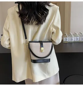 Detail of a beige canvas bucket bag with black leather trim and gold metal clasp