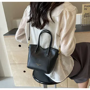Detailed back view of a minimalist black leather tote bag worn by a model in a cozy room