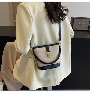 Detail of canvas bucket bag with black leather trim and golden metal clasp on a model