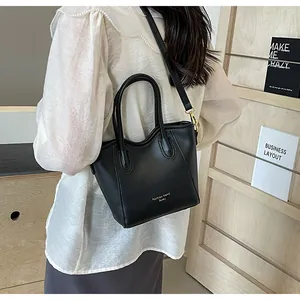 Detail of a black leather crossbody bucket bag with dual handles and gold brand lettering