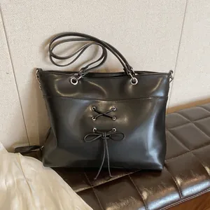 Black ballet-style large tote bag with ribbon bow and metal eyelets on a brown leather bench