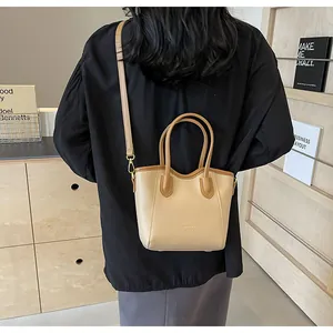 Rear view of model holding a beige and brown contrast tote bag with adjustable strap