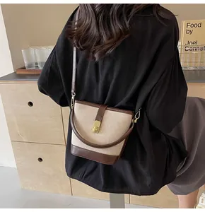 Detail of canvas bucket bag with brown leather trim and golden metal twist lock closure