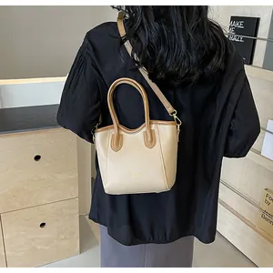 Detail of two-tone tote bag featuring beige leather body and adjustable shoulder strap