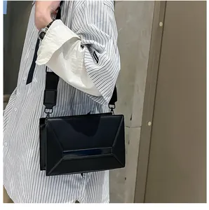 Close-up of black geometric crossbody bag with glossy leather texture and wide strap