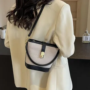 Chic beige canvas and black leather bucket bag worn by model in a minimalist setting