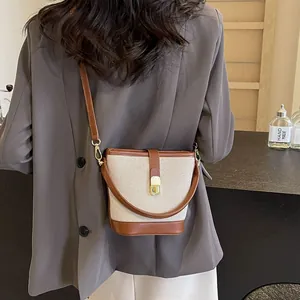 Contrast canvas bucket bag with brown leather trim and metal clasp worn over the shoulder