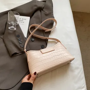 Pink croc-embossed baguette shoulder bag with silver studs on a minimalist bed setting