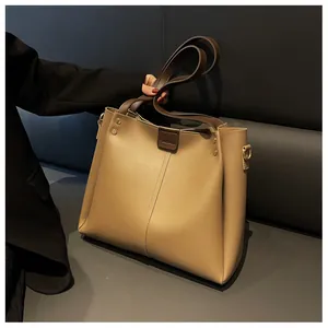 Detail of khaki tote bag with dark brown handles and brand logo on minimalist sofa