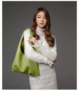 Close-up of grass green pebbled leather hobo bag worn by a model in a white lace shirt