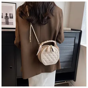 Détail du sac rond beige matelassé avec poignée foulard sur un modèle en blazer