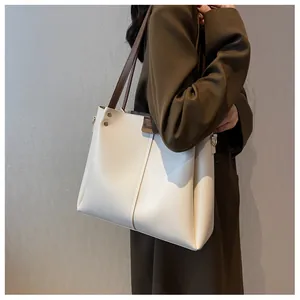 Macro detail of the creamy white leather tote bag showing golden studs and brown straps