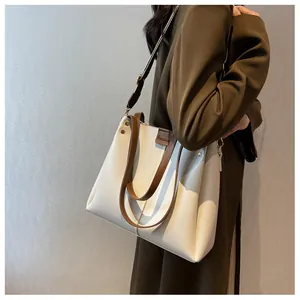 Detail of a large cream tote bag with brown straps and logo patch worn by a model