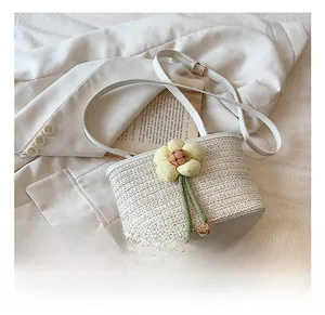Detail of woven straw bucket bag featuring a knit sunflower charm and cream leather strap