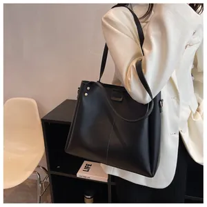 Detail of black faux leather tote bag with gold rivets and elegant white tweed jacket