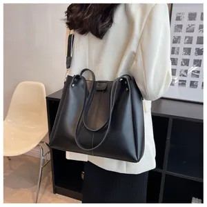 Detail of a large black matte leather tote bag featuring a wide shoulder strap and metal rivets