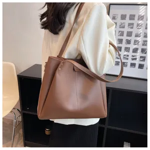 Detail view of large dark brown leather tote bag with wide shoulder strap on a model