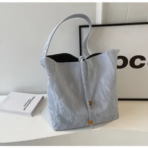 Detalle del bolso tote plisado azul claro con cierre de cordón y cuentas amarillas decorativas