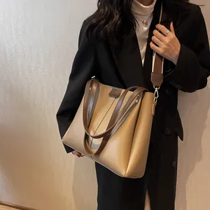 Large capacity khaki tote bag with wide strap, worn by a model in a black suit