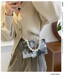 Detail of a marble-textured hard shell box bag with pearl handle and gold chain strap