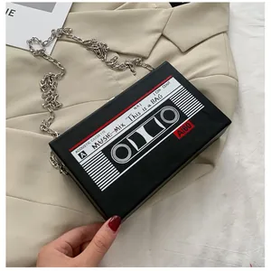Retro cassette-shaped black crossbody bag with silver chain strap on beige blazer