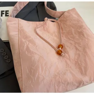 Detalle del bolso tote rosa con textura arrugada, cuentas de ámbar y correas finas