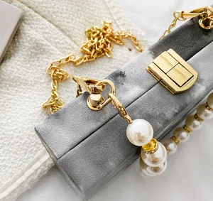 Close-up of golden metal clasp and pearl charm detail on a gray textured box bag