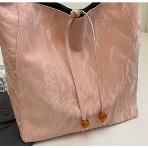 Detalle del bolso tote rosa claro plisado con cordón de cuentas de ámbar y textura brillante