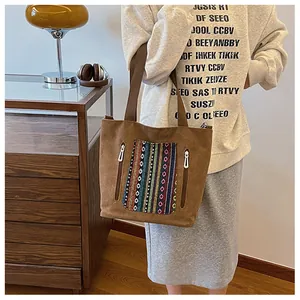 Detail of a brown canvas tote bag with ethnic embroidery and vertical dual zippers