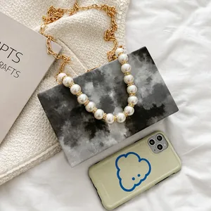 Detail of marble pattern box bag with pearl handle and gold chain next to a phone