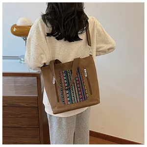 Close-up of a brown canvas tote bag with colorful ethnic embroidery shown on a model