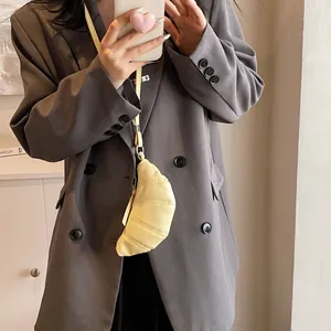 Crossbody view of a pale yellow croissant bag on a model wearing a grey blazer