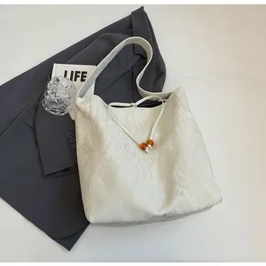 Detalle del bolso tote blanco con textura plisada y cordón con cuentas de madera en blazer