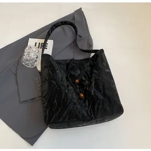 Detalle del bolso tote de cuero arrugado brillante negro con cuentas de ámbar decorativas