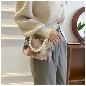 Detail of marble pattern crossbody bag with pearl handle and golden chain strap