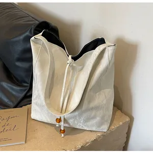 Detalle de bolso tote blanco con textura arrugada, cordón y cuentas de ámbar