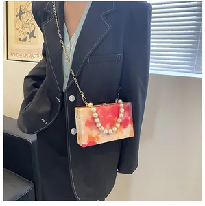 Detail of red marble acrylic box bag featuring gold chain and white pearl handle