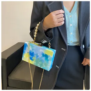 Macro detail of hand-painted box bag featuring pearl handle and gold chain strap