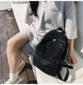 Dettaglio dello zaino in denim nero lavato con cuciture bianche e tasca anteriore con zip