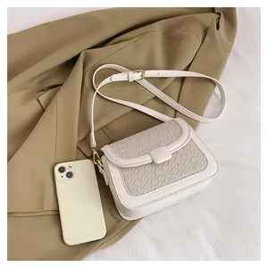 Close-up of the elegant woven texture and golden metal buckle on a cream crossbody bag