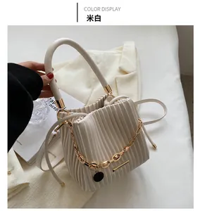 Détail du sac seau plissé blanc crème avec chaîne dorée et pendentif noir élégant