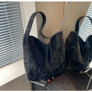 Detalle de bolso tote hobo plisado negro con cierre de cordón y adornos de cuentas ámbar