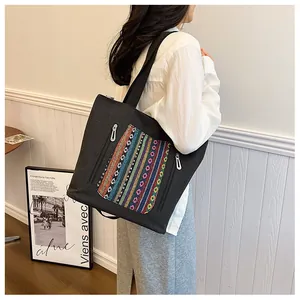 Detailed close-up of a black canvas tote bag with bohemian embroidered pocket and silver zippers