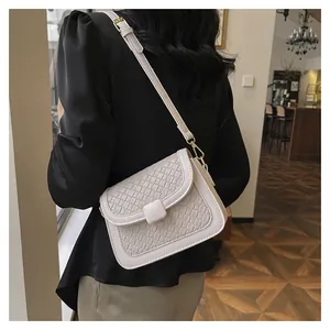 Close-up of beige crossbody bag with woven texture flap and gold metal hardware hooks