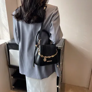 Détail du sac seau plissé noir avec chaîne dorée porté par un mannequin en gris
