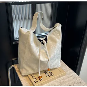 Detalle de bolso tote plisado blanco crema con cierre de cordón y cuentas ámbar