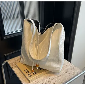Detalle del bolso tote blanco con textura arrugada, cordón y adornos de cuentas de ámbar