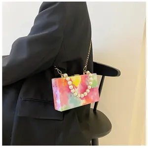 Detail of colorful printed box bag featuring a pearl handle and gold chain strap